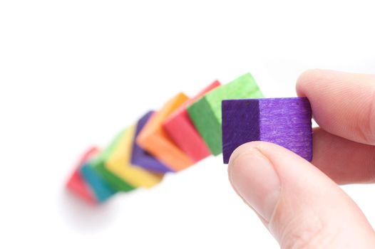 Male fingers building with colourful toy wooden blocks in a concept of development and expansion, or as a learning tool to teach kindergarten children coordination