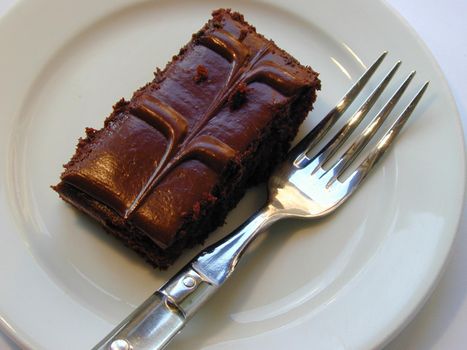 Delicious portion of rich glazed chocolate cake with a decorative patterned icing served on a white plate with a fork for tea, high angle view