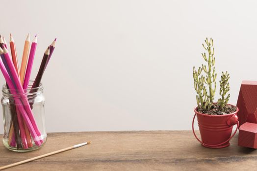 Designers desk or workspace with copy space with colored pencils in a glass jar, paintbrush and potted plant against a white wall