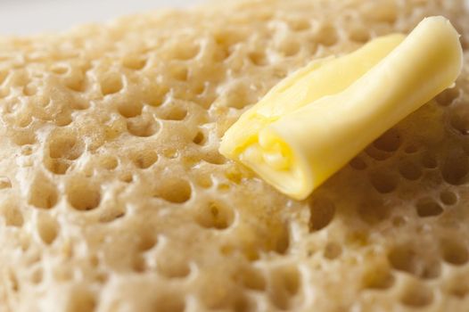 Melting curved slice of yellow butter on top of delicious hot crumpet, bread or pancake