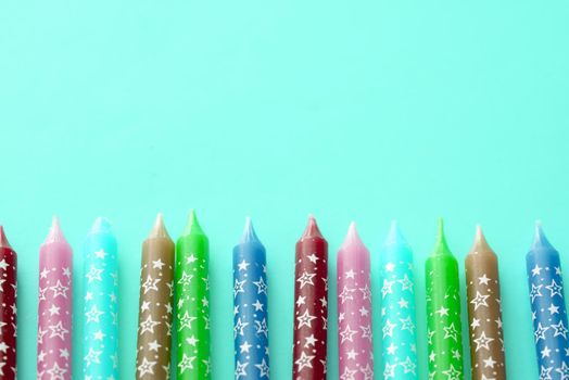 Row of birthday candles decorated with stars and colored green, maroon, blue, lavender against an aqua background