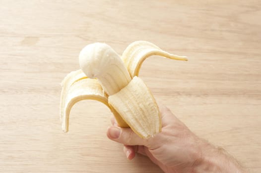 a hand holding a peeled half eaten banana with wood background