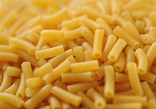 Macaroni background texture with a heaped pile of dried macaroni pasta in a shallow DOF view for use in Italian cuisine