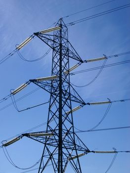 Detail of the top of an electricity pylon, showing all the connecting cables, against a clear blue sky