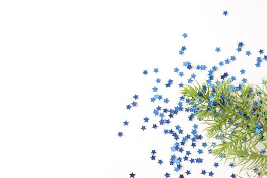 Sprig of Evergreen Tree Branch on White Background with Blue Star Shaped Glitter Confetti, Christmas Themed Image with Copyspace for Text
