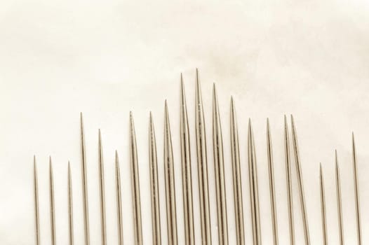 Close up on set of various sized sewing needle points organized by height and thickness over paper