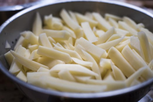 Sliced fresh potatoes in a metal bowl ready to make French fries or fried chips, close up view