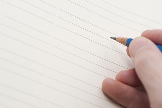 Male hand holding a pencil ready to commence writing on a blank lined sheet of paper