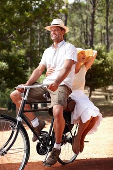 Casual countryside cycling. Playful couple having fun while riding on retro bicycle together