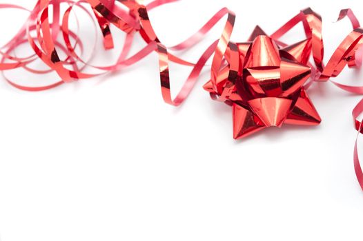Metallic red foil ornately tied bow and twirled ribbon used to decorate Christmas gifts lying on a white background with copyspace