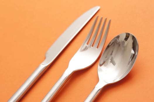 Close Up of Set of Silver Cutlery Dinner Service Including Spoon, Fork, and Knife on Orange Background