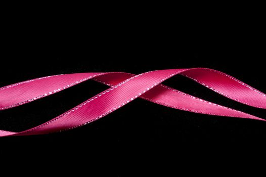 Twirled pink ribbon festive border on a dark background with copy space above and below for your greeting