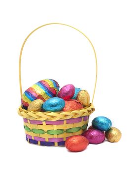 A decorative basket filled to overflowing with colourful foil wrapped Easter Eggs on a white background
