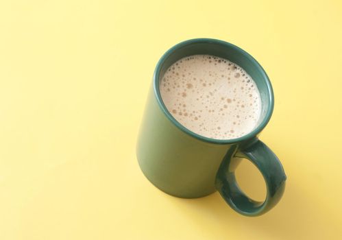 Green mug of vanilla cappuccino or cafe latte, high-angle close-up on yellow