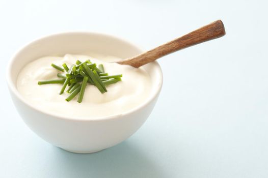 Bowl of sour cream garnished with fresh chopped chives with a small wooden spoon for serving, with copy space