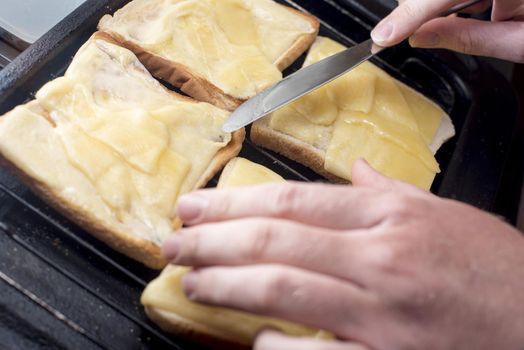 Hands with blunt knife handle toast and cheese melting on four slices of white bread on grill