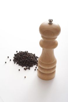 Heap of black peppercorns with a wooden pepper mill or grinder over a white background with copy space