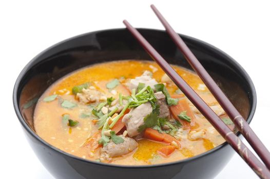 Delicious bowl of Peranakan cuisine laksa soup with meat, herbs, carrots and chopsticks on top