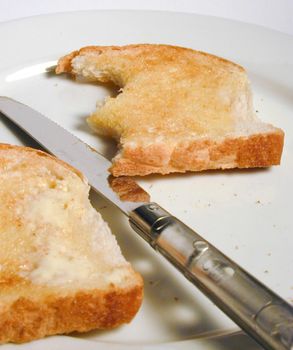 Buttered slices of white toast on a plate with a knife with one slice missing two bites