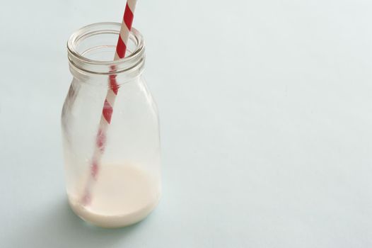 Lone glass bottle nearly emptied of white milk and having a single striped straw