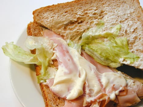 Preparing a sandwich for lunch with thinly sliced ham and lettuce on brown bread, closeup view