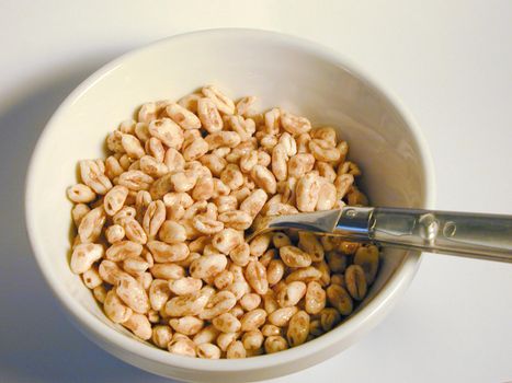 High angle view of commercial puffed wheat breakfast cereal in a white ceramic bowl with a spoon