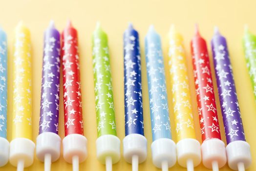 Colorful row of birthday cake candles in the colors of the rainbow decorated with festive stars on a yellow background