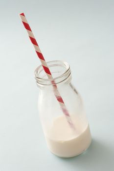 Creamy milk fills bottom of short glass bottle with stripped straw against a light colored background