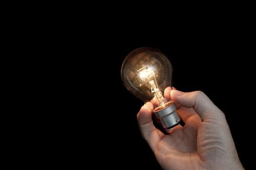 a hand holding a glowing light bulb with a black background