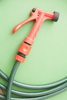 Garden red plastic spray nozzle attached to a green coiled hose pipe for spraying a fine jet of water on seedlings and delicate plants