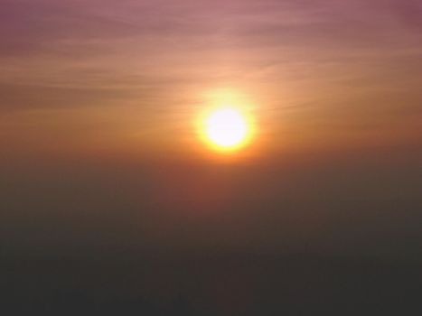 Sun setting in a hazy smoggy polluted sky with muted blended colours of orange and purple