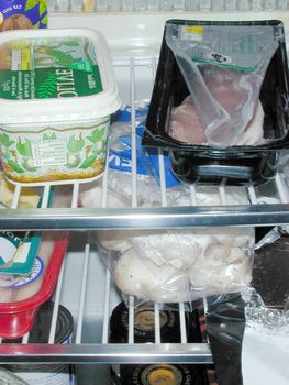 Contents of refrigerator with various groceries in commercial and home packaging on wire metal shelves