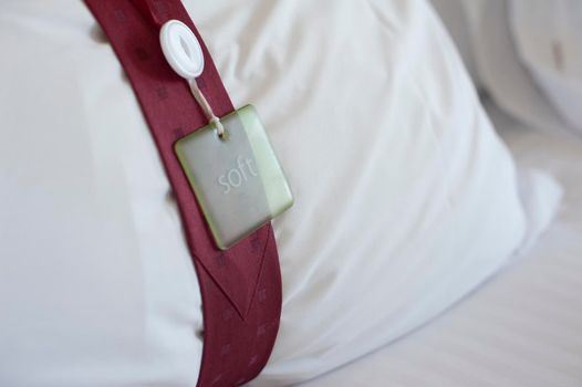 Hotel bedroom pillow with a decorative band tied around it with an attached tag, close up view conceptual of the hospitality industry