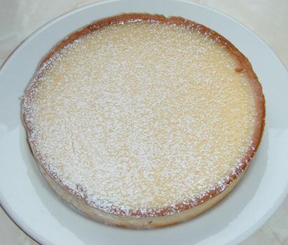 Baked pie in a crispy pastry crust sprinkled with icing sugar and served on a white plate, high angle view