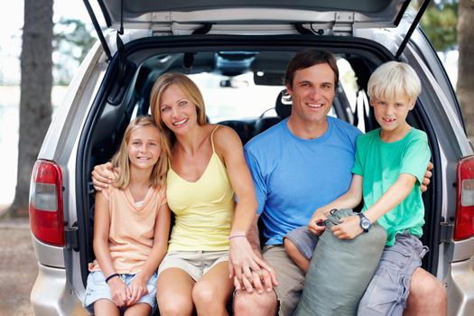 Attractive family sitting in the back of a car and smiling. Portrait of an attractive family of four sitting in the back of a car and enjoying their vacation