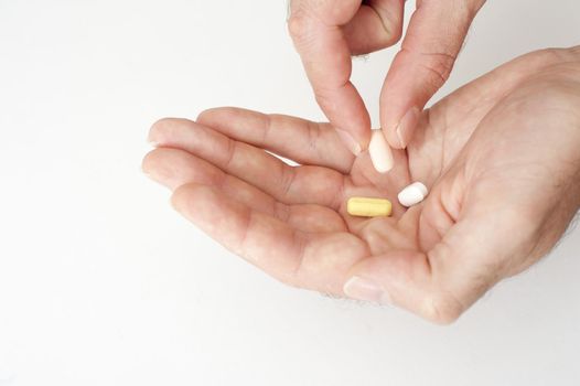 Person taking medication lifting a tablet from a cocktail of three in his hand in a healthcare concept, close up over a white background