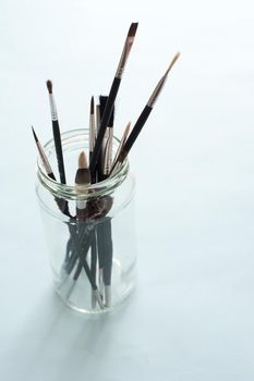 Glass jar with assorted paintbrushes in different sizes and shapes of bristle for art, high angle over a grey background