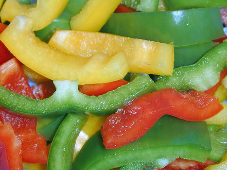Food or catering background of sliced colorful sweet bell peppers in green, red and orange for use in a healthy fresh salad or as a flavoring in cooking