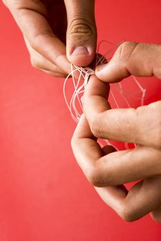 Untangled concept with man unravelling a knot in fine twine with his fingers over a red background with copy space