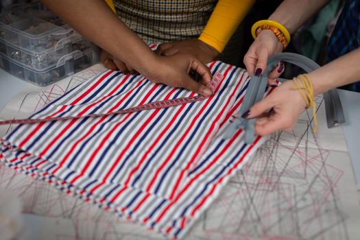 The striped fabric is lying on the tailor's table and the seamstress is measuring whether she has enough to sew the dress. Two African women and a European woman in a tailor's shop.