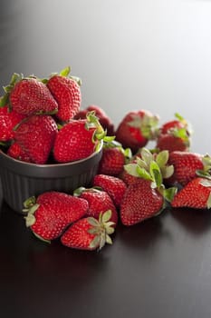 Bowl of fresh succulent ripe red strawberries overflowing onto a dark table on a graduated grey background with copyspace