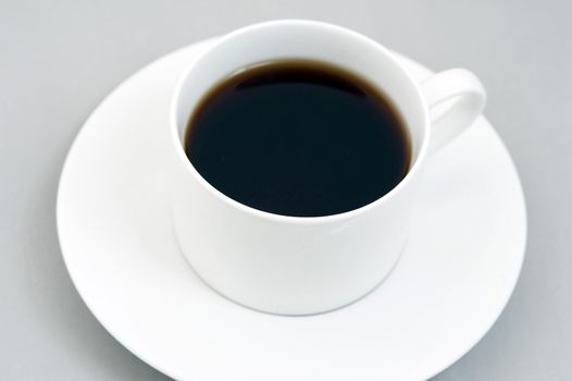 Cup of black espresso on white saucer. Grey background