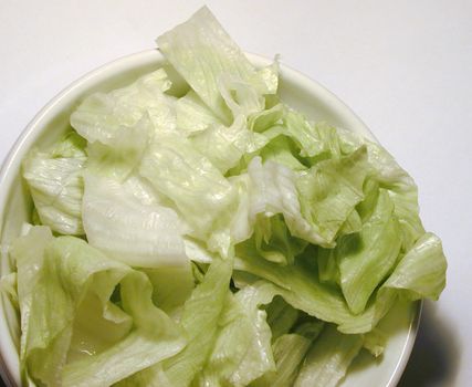 Closeup of a white bowl of shredded iceberg lettuce over white background