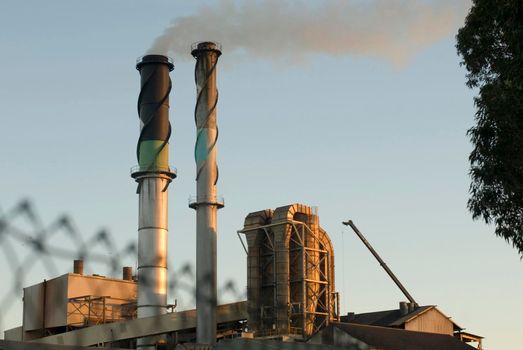 View of a factory or refinery with two tall chimneys spewing smoke into the atmosphere causing industrial air pollution