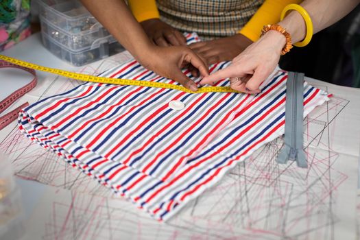 Matching the button to the fabric. Index finger. Hand of a dark-skinned woman and a European woman. The background of a tailor's workshop.