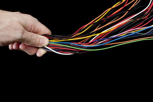 Multiple multicoloured electric wires in a diverging tangle are constrained and controlled under the thumb of a man