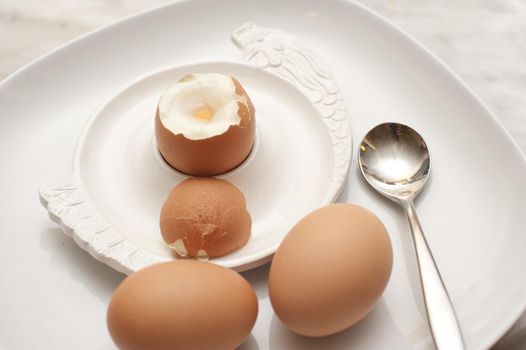 Serving of three boiled eggs for breakfast with two eggs on the side and the third soft-boiled egg with its top cut off in an eggcup
