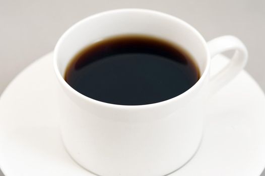 Black energizing coffee served in a white round cup on a saucer made of porcelain, close-up