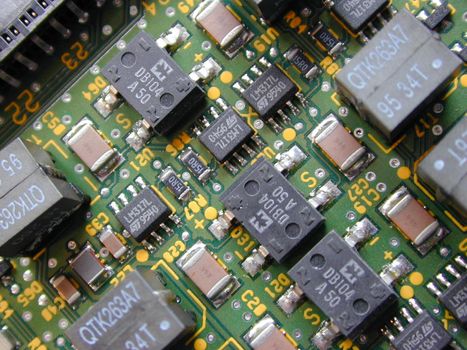 Close up of diode rectification, transformer and transistor electrical components on a green circuit board.