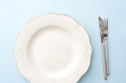 Clean empty white dinner plate on a table with cutlery alongside viewed from overhead in a food and catering concept